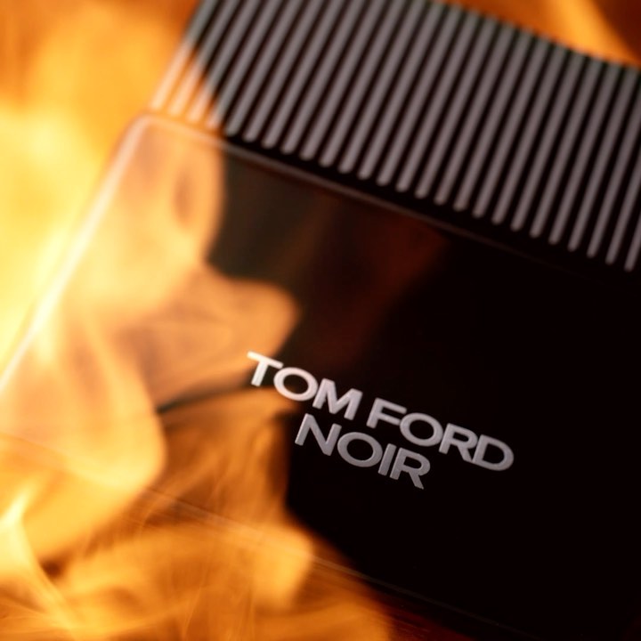 Close-up of Tom Ford Noir perfume bottle against a fiery orange background with a dark bottle top and the brand and product name.
