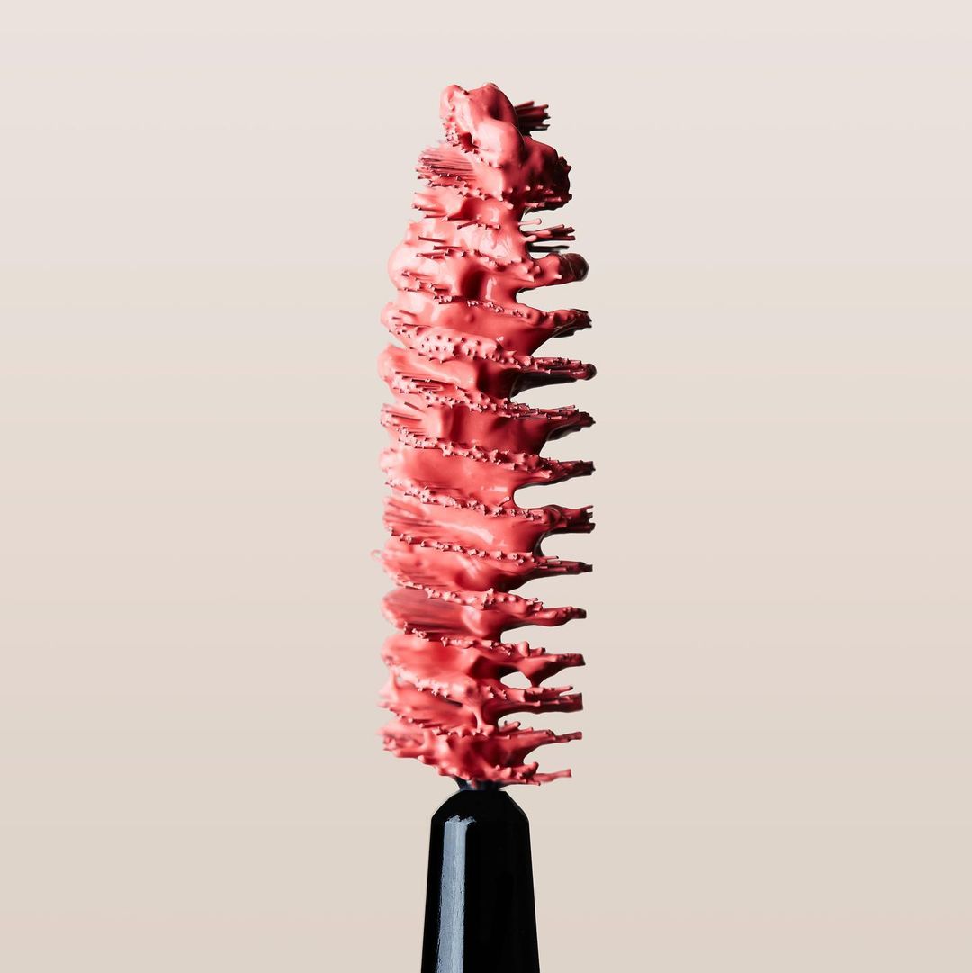 Close-up of a pink mascara wand showing texture of the product, studio shot on neutral background, beauty product photography.