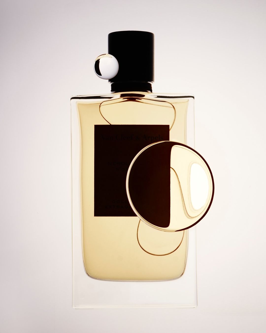 High-angle studio shot of a perfume bottle with a black cap and label, along with two geometric decorative spheres against a bright background.