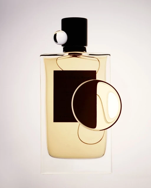 High-angle studio shot of a perfume bottle with a black cap and label, along with two geometric decorative spheres against a bright background.