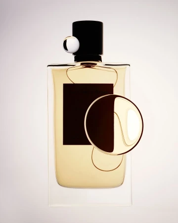 High-angle studio shot of a perfume bottle with a black cap and label, along with two geometric decorative spheres against a bright background.