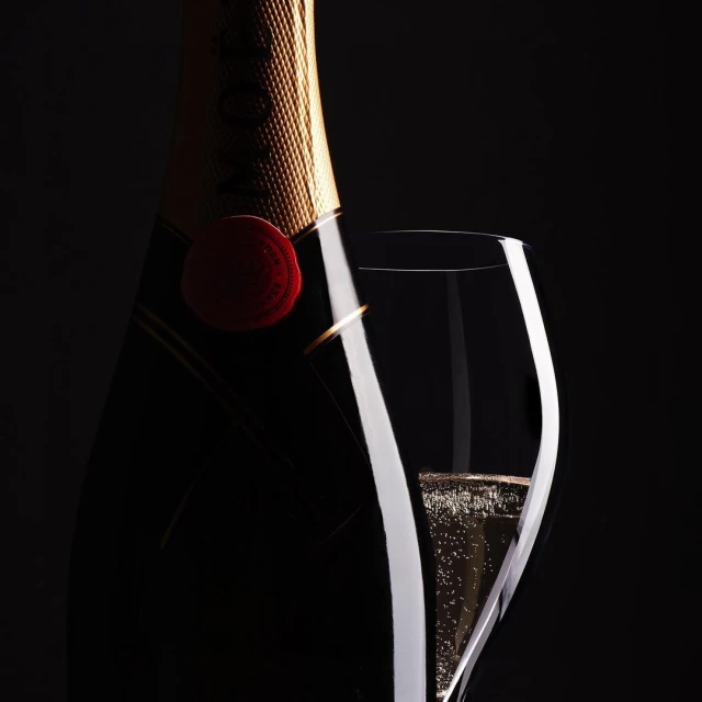 Dramatic close-up of a champagne bottle and glass filled with champagne, set against a dark background, highlighting the drink's elegance.