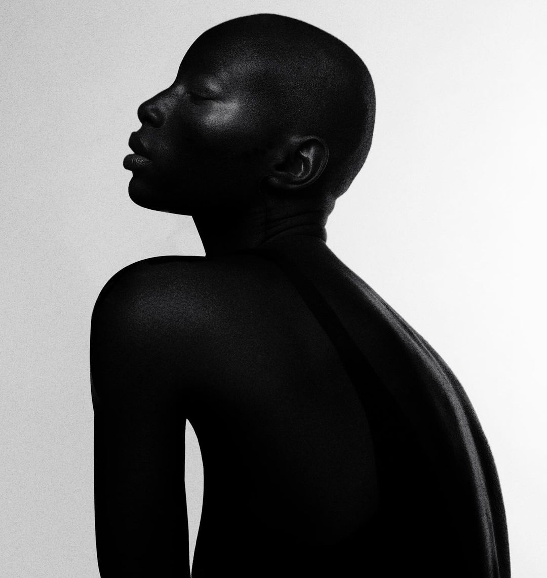 Striking black and white portrait of an African adult female with shaved head, smooth skin, and closed eyes against a plain white backdrop.