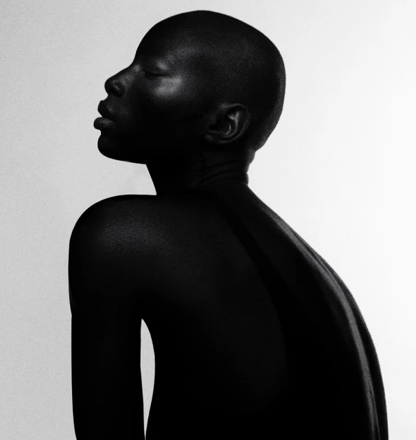 Striking black and white portrait of an African adult female with shaved head, smooth skin, and closed eyes against a plain white backdrop.