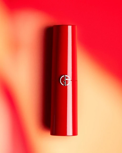 Red lipstick with a silver 'GA' logo is centered on a blurred background transitioning from red to orange in vertical product shot.