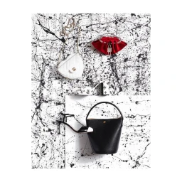 Overhead flat lay of luxury fashion accessories including white heart bag, red pouch, and black bucket bag arranged on a black splatter backdrop