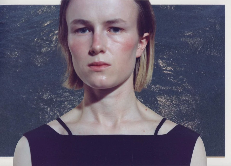 Portrait of a woman with short blonde hair wearing a black top, against a backdrop with a marbled, dark blue texture.