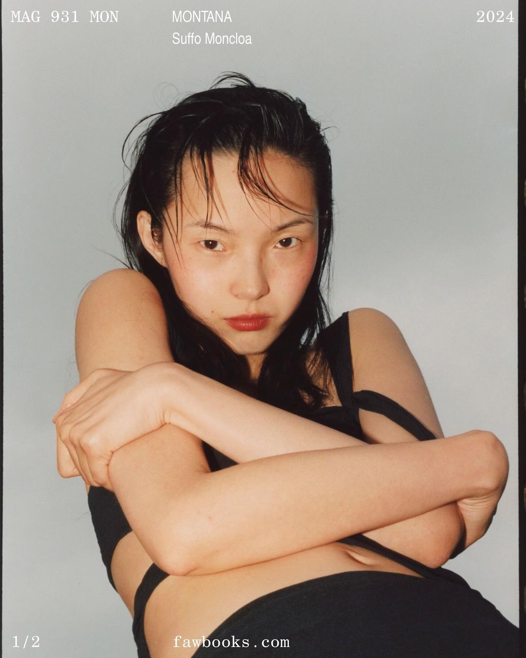 Young woman with slicked-back dark hair poses with arms crossed in a black top against a light blue background for a magazine cover.
