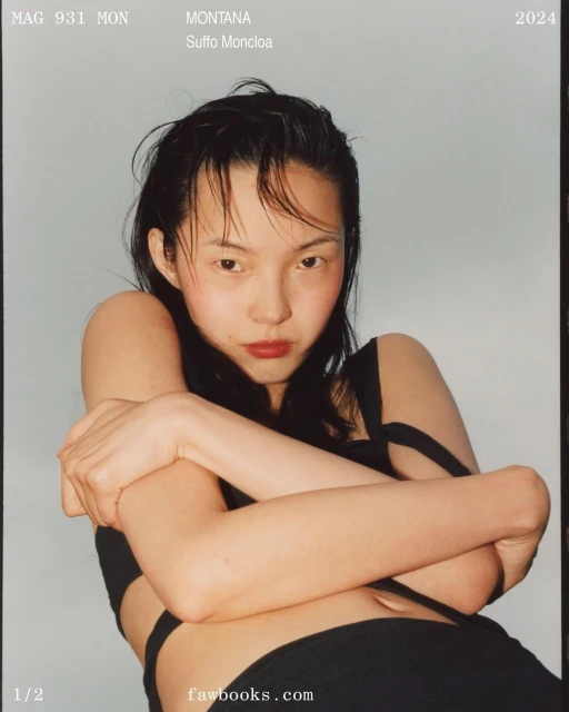 Young woman with slicked-back dark hair poses with arms crossed in a black top against a light blue background for a magazine cover.