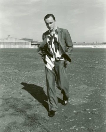 Man walking outdoors wearing a suit jacket and patterned shirt against an open horizon by Suffo Moncloa