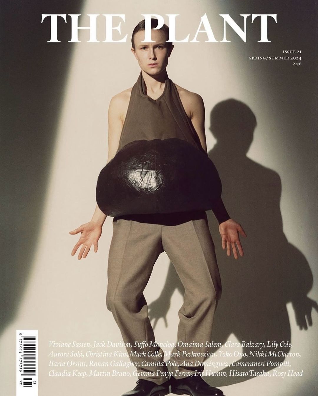 Magazine cover featuring a model wearing a halter top and trousers, posing with a large, black sculptural object in front of a white background.