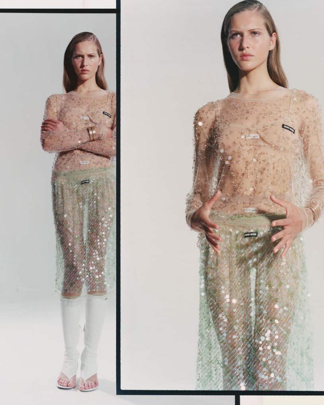 Fashion shot of a slender woman in a sheer, embellished long-sleeved dress with white boots, posing against a neutral studio background with reflection.