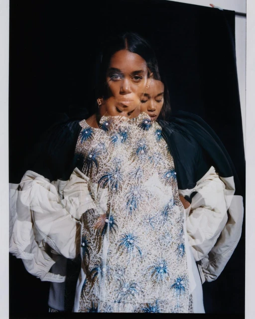 Studio portrait of a woman wearing a patterned top against a black background with a double exposure effect.