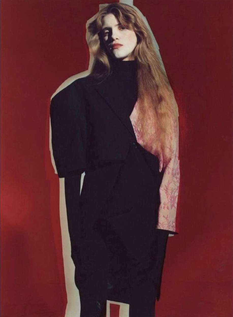 Fashion editorial shot of a woman with long red hair wearing a black dress against a bold red background with a cutout shadow.