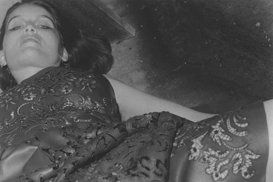 Monochrome portrait of a woman in patterned dress, lying down. The low-angle shot highlights her face and the intricate design of the fabric.