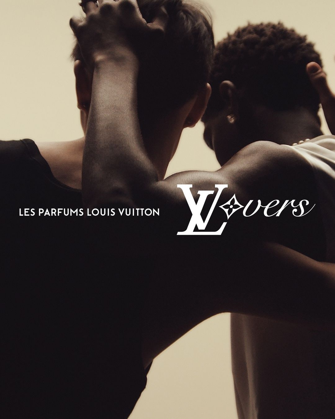 Advertisement for Les Parfums Louis Vuitton showing two young adult men with dark hair standing close together in a neutral indoor setting.