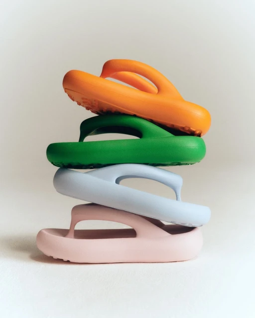 Stack of four colorful platform flip-flops in orange, green, blue, and pink on a plain background, showcasing summer footwear fashion.