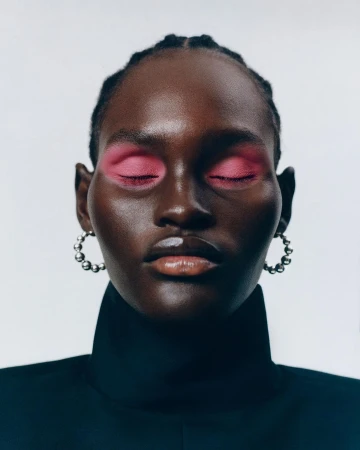 Close-up beauty portrait of a Black woman with bright pink eyeshadow, beaded silver hoop earrings, and a black high-collar garment.
