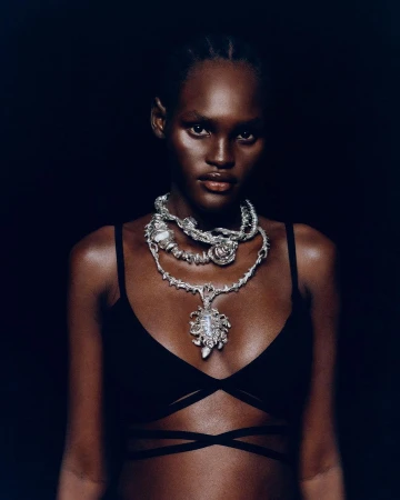 Black woman wearing a black top and layered silver statement necklaces against a dark background