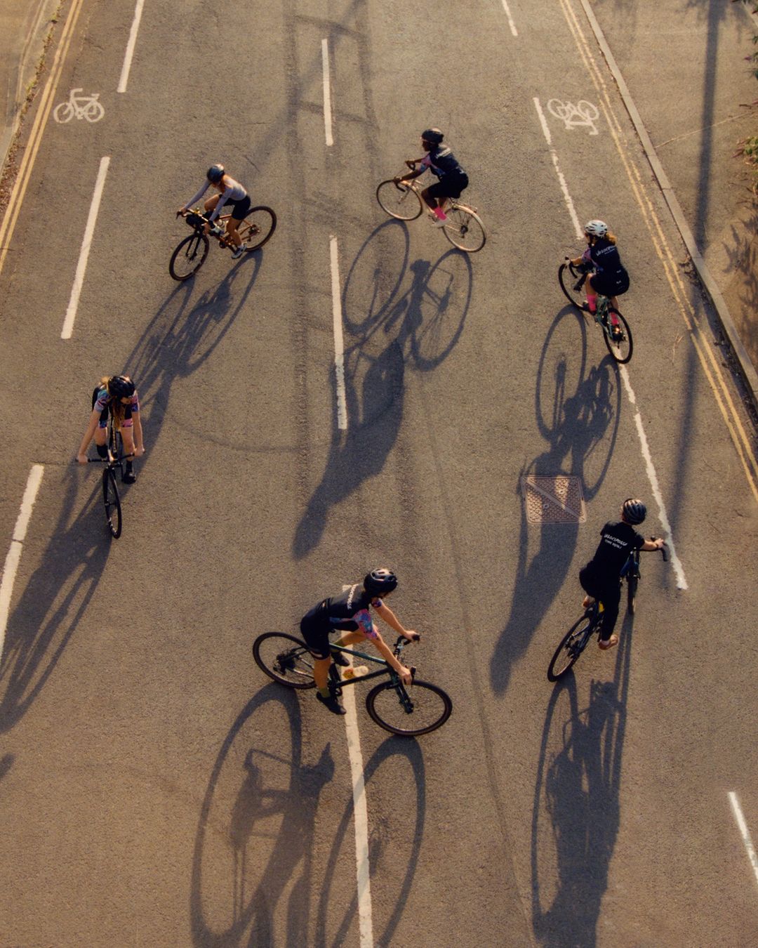 Overhead shot of a group of cyclists riding bicycles on an urban road with lane markings and bicycle lane symbols painted on the asphalt.