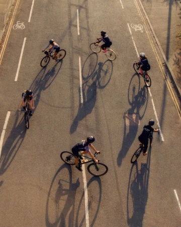 High-angle overhead view of five cyclists riding bicycles along an asphalt city street with long cast shadows.