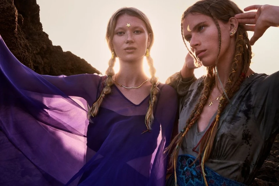 Two fair-skinned adult female models in outdoor setting. The model on the left wears a purple dress with a gold star on her forehead.