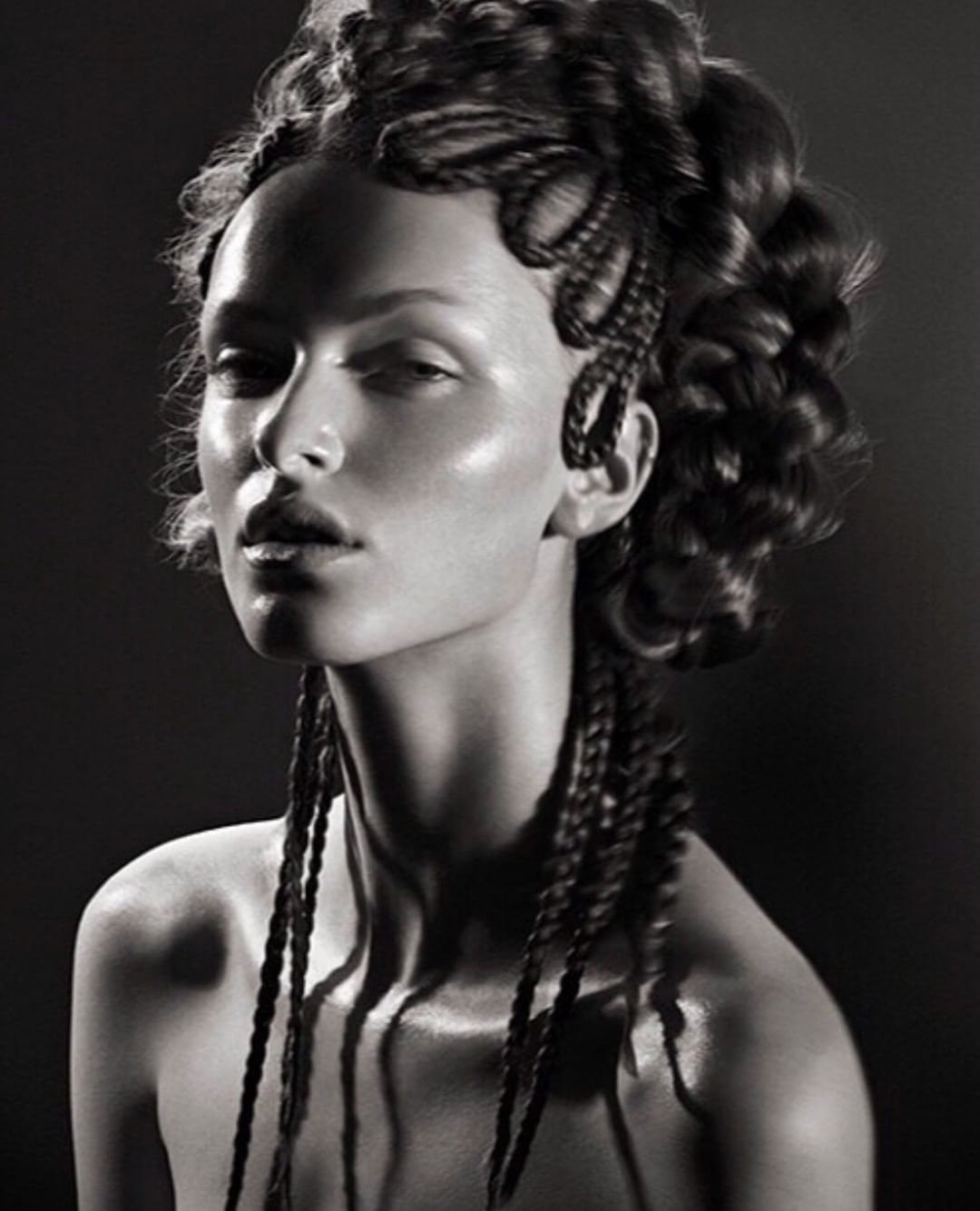Striking black and white beauty portrait of a young adult female model with unique braided hair and flawless, dewy skin in a studio setting.