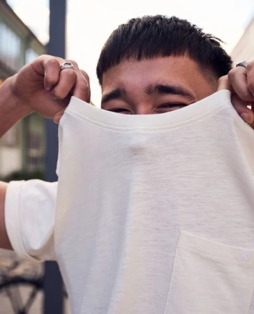 Close-up portrait of a young man pulling up a white t-shirt to cover his face, photographed by Sune Czajkowski in London.