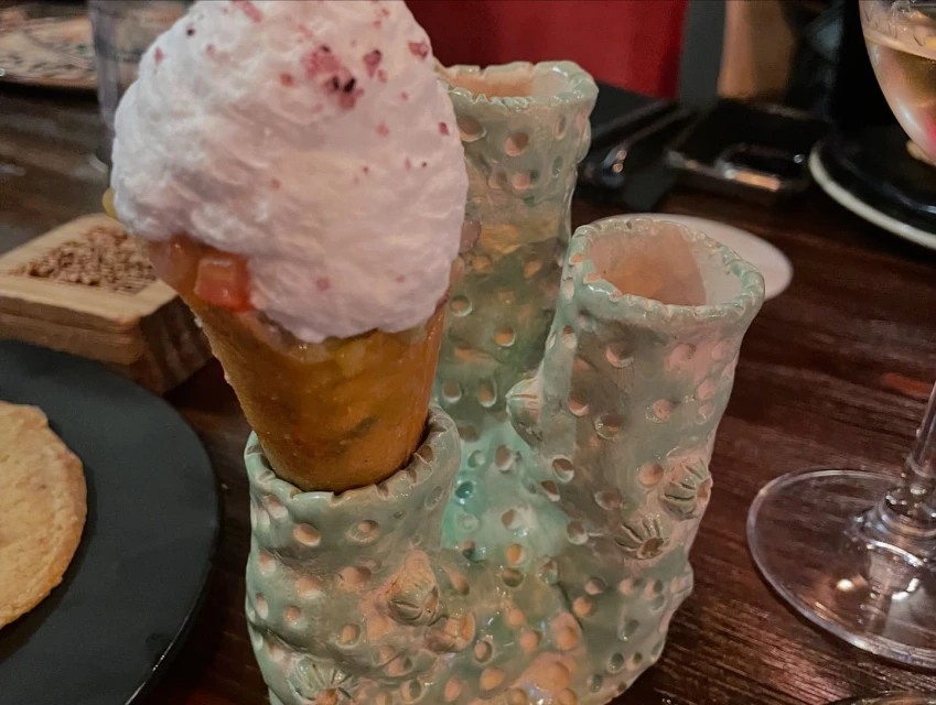 Dessert cone with white whipped cream and light pink sprinkles served in a light green ceramic holder with a dark wood table.