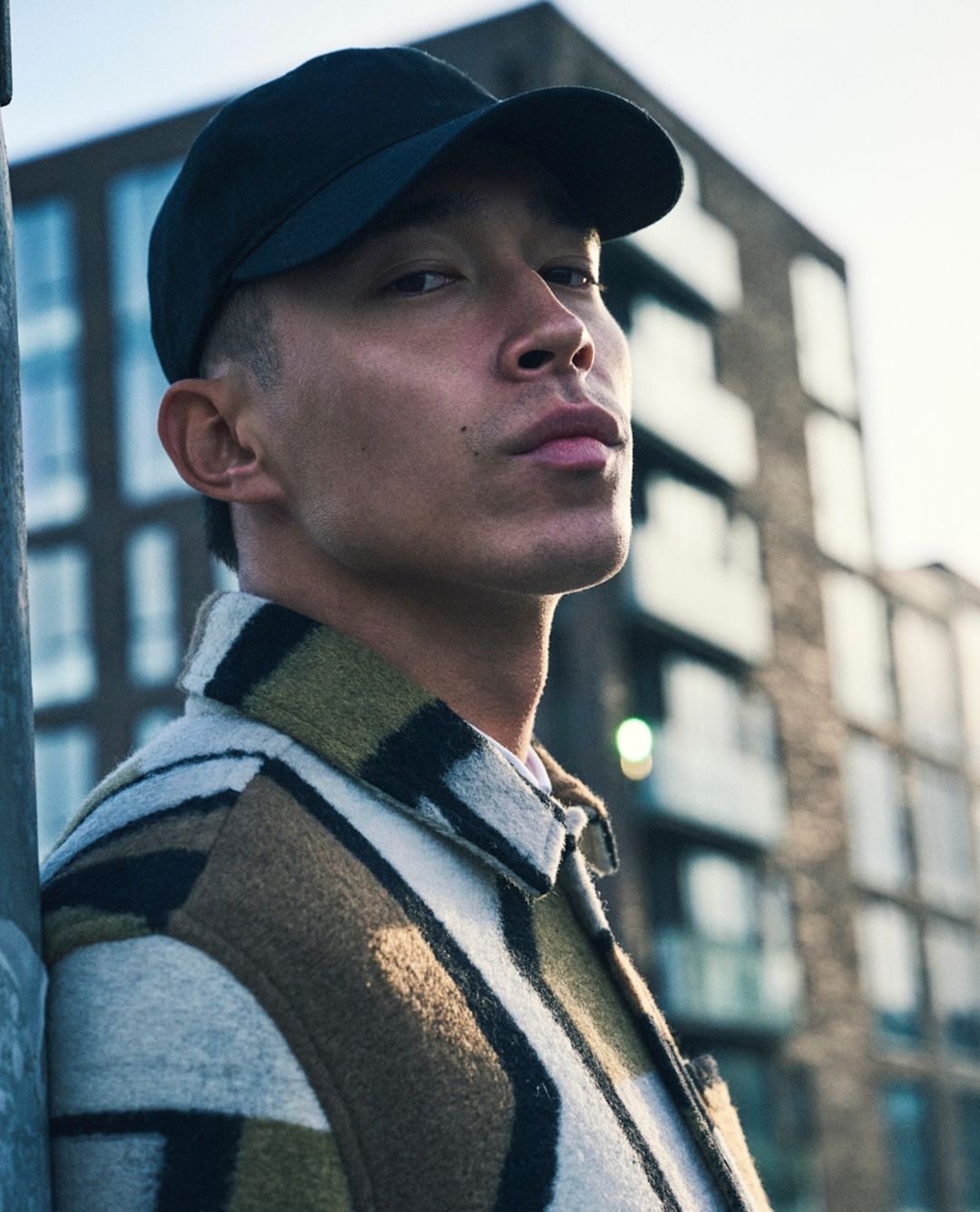 Man wearing a black baseball cap and patterned jacket looking down outdoors in London by Sune Czajkowski.