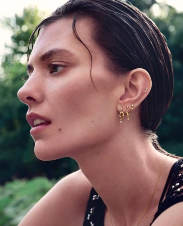 Close-up portrait of a woman with slicked-back wet hair wearing gold earrings and a dark embellished top outdoors in London.