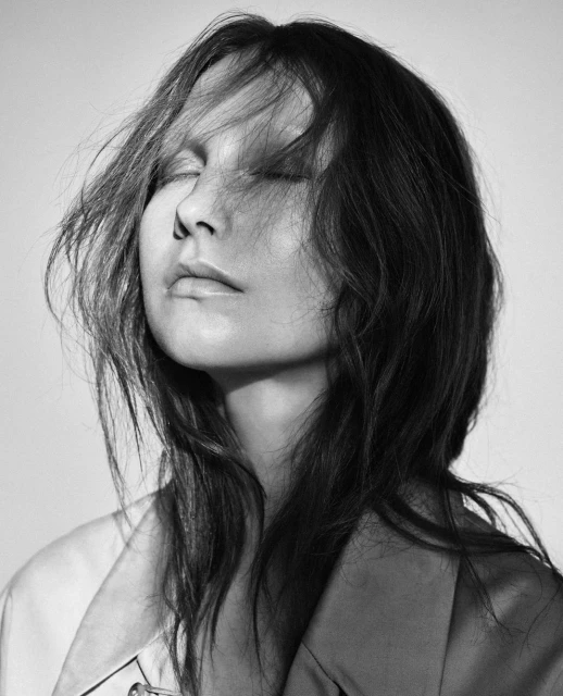 Monochrome portrait of an adult female with eyes closed and windswept hair in a photo studio with a soft light and shallow depth of field.