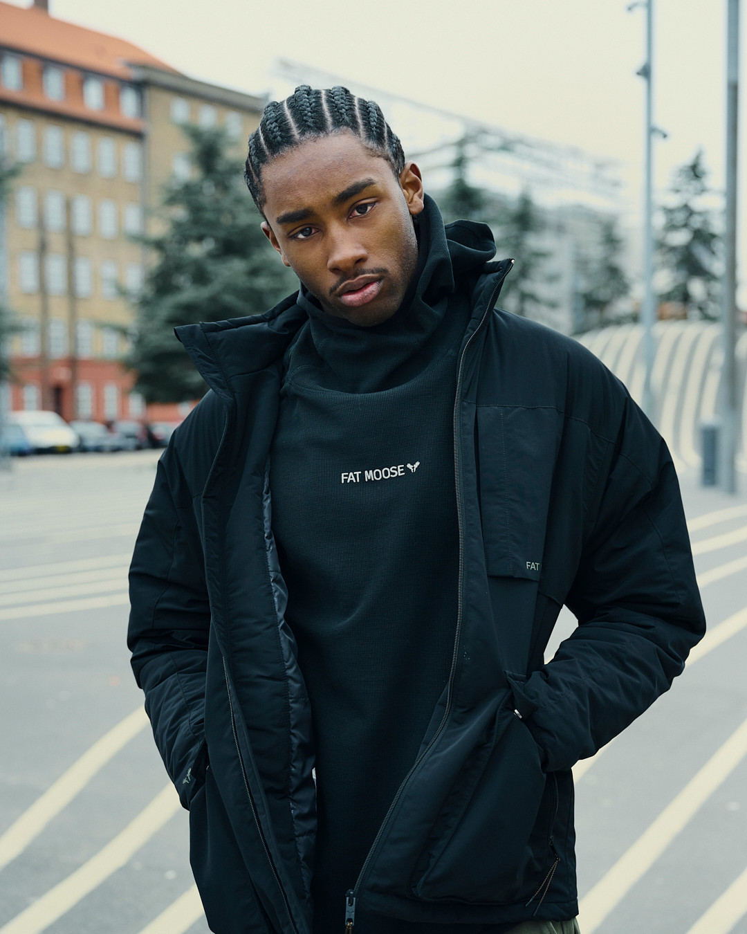 Portrait of a handsome Black man in a black Fat Moose jacket standing outdoors with a building and street in the background.