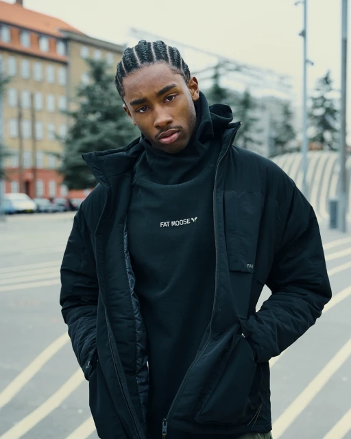 Portrait of a handsome Black man in a black Fat Moose jacket standing outdoors with a building and street in the background.