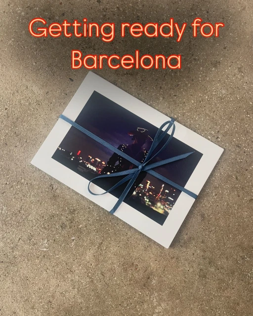 Cityscape photo print tied with blue ribbon displayed on a textured surface, evoking travel or gift-giving concept.