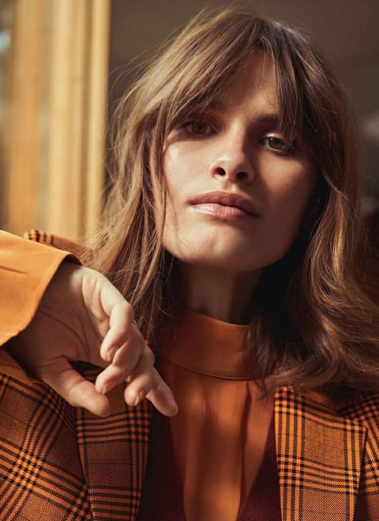 Close-up portrait of a woman with bangs wearing an orange plaid jacket photographed in London by Sune Czajkowski.