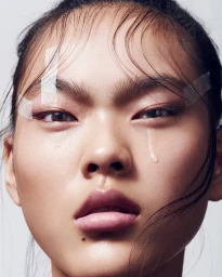 Close-up beauty portrait of an East Asian woman with tape on her forehead and a faux tear on her cheek by Sune Czajkowski
