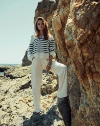 Woman wearing a striped sweater and white trousers posing on rocky terrain by the ocean by photographer Sune Czajkowski.