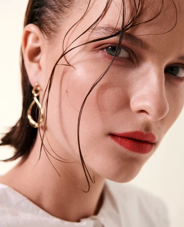 Close-up portrait of a woman with wet hair wearing a gold drop earring and red lipstick by Sune Czajkowski