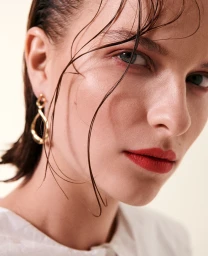 Close-up portrait of a woman with wet hair wearing a gold drop earring and red lipstick by Sune Czajkowski