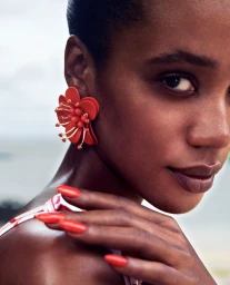 Close-up portrait of a Black woman wearing a large red floral earring and matching red nail polish by Sune Czajkowski.