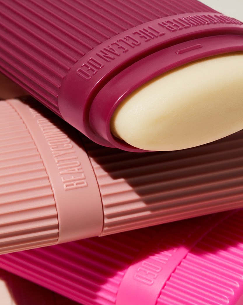 Three colorful deodorant sticks in pink and magenta hues are stacked at a slight angle, showcasing a minimalist beauty product design.