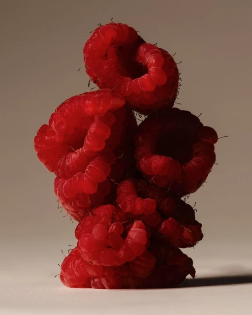 Close-up studio shot of a vibrant, textured stack of fresh red raspberries against a neutral background, showcasing their form and color.