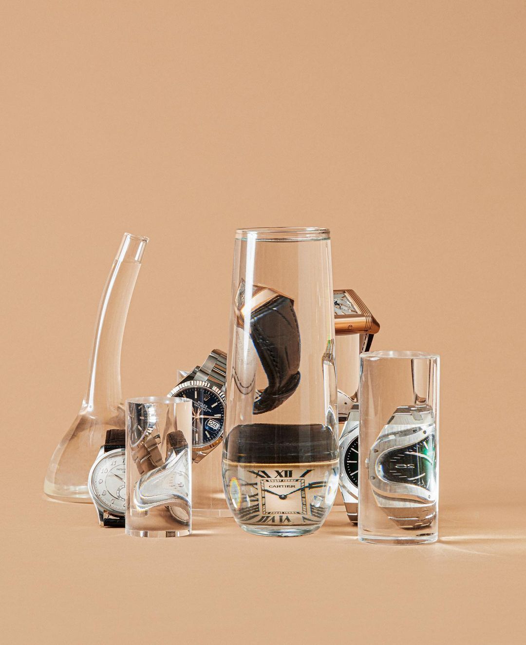 Conceptual studio shot of six wristwatches in glass containers against a neutral background. Watches have silver, gold, and leather bands.
