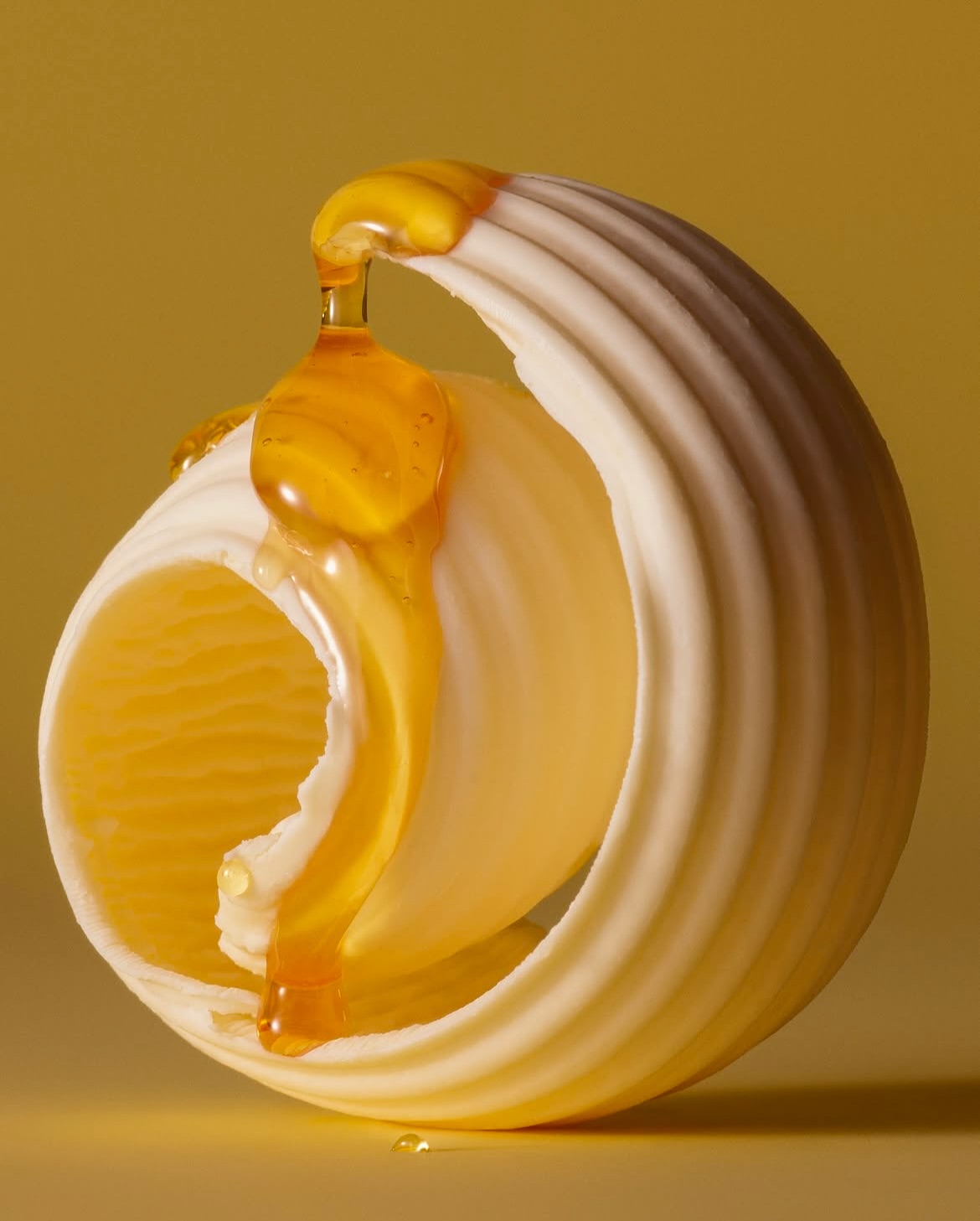 Close-up studio shot of lumaconi pasta with honey dripping, set against a yellow background, highlighting the texture and warm color palette.