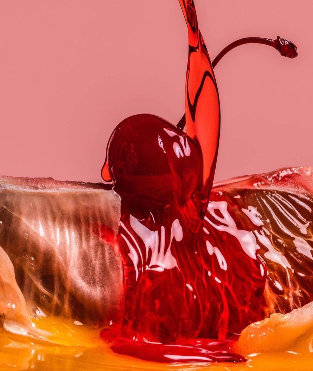 Close-up of a cherry with juice pouring onto a slice of citrus fruit, studio shot on a pink backdrop; food and beverage concept.