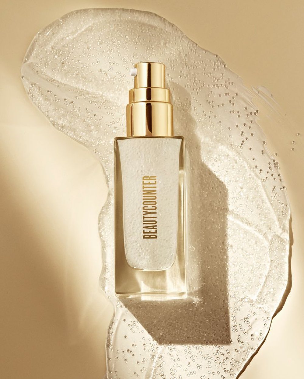 BeautyCounter skincare product in a clear bottle with a gold lid on a background of translucent gel, studio shot for advertising.