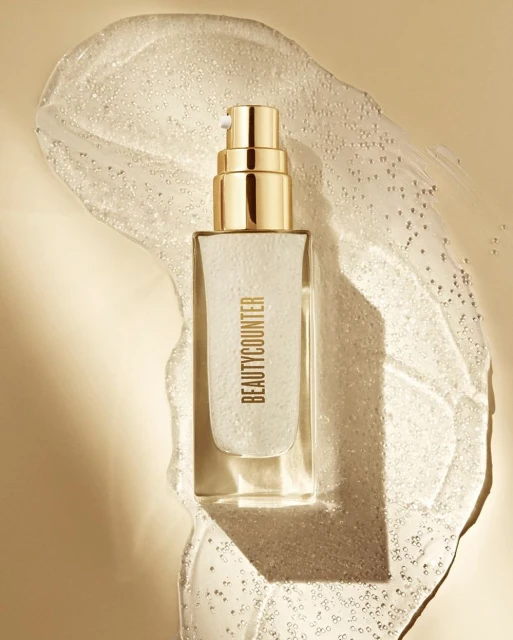BeautyCounter skincare product in a clear bottle with a gold lid on a background of translucent gel, studio shot for advertising.
