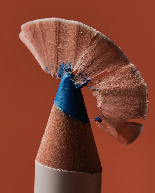 Close-up of a blue makeup eyeliner pencil with the wood shavings at the tip set against a solid orange backdrop.