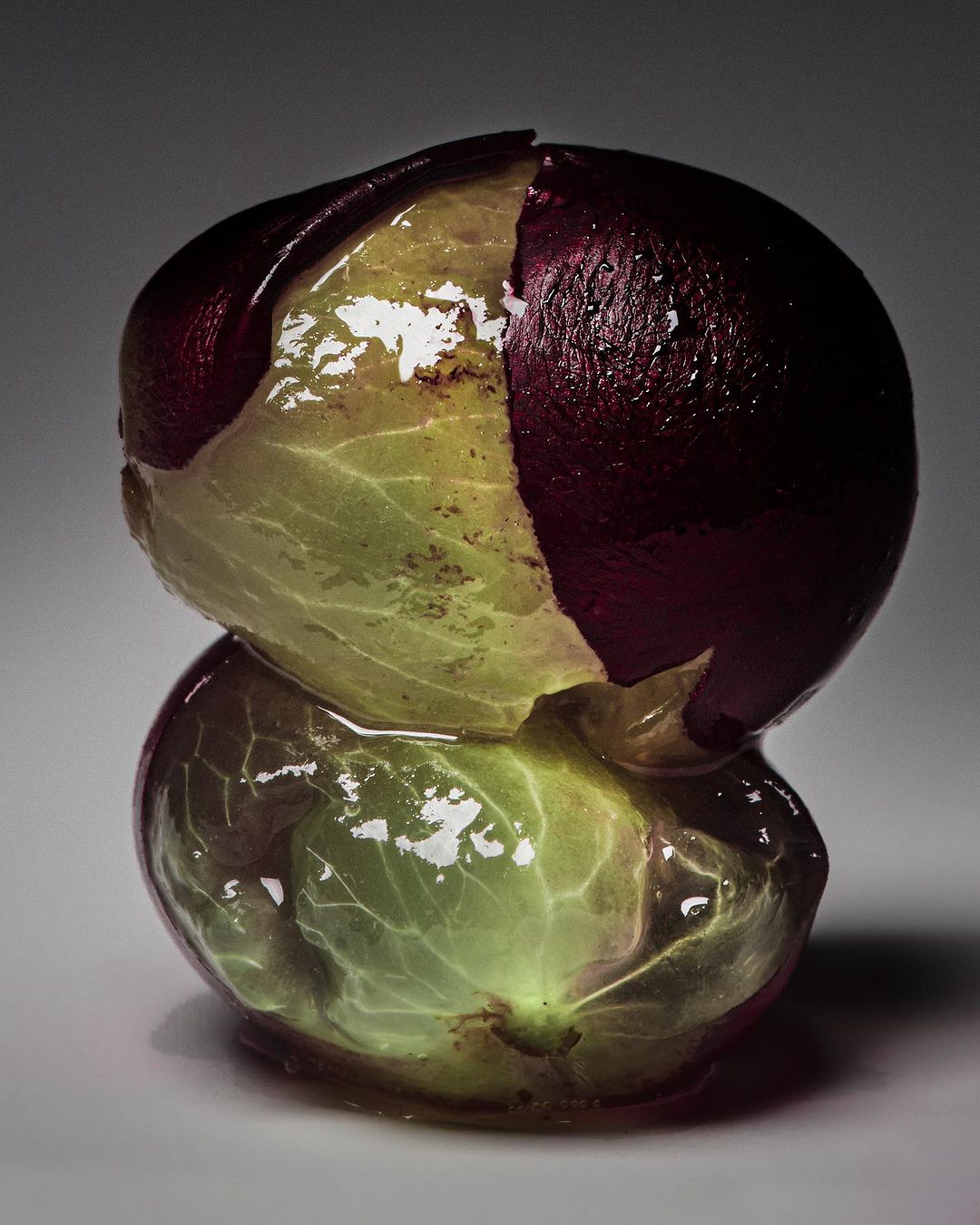 Macro photograph of two grapes, one stacked on top of the other, featuring a partially peeled skin revealing the translucent fruit inside.